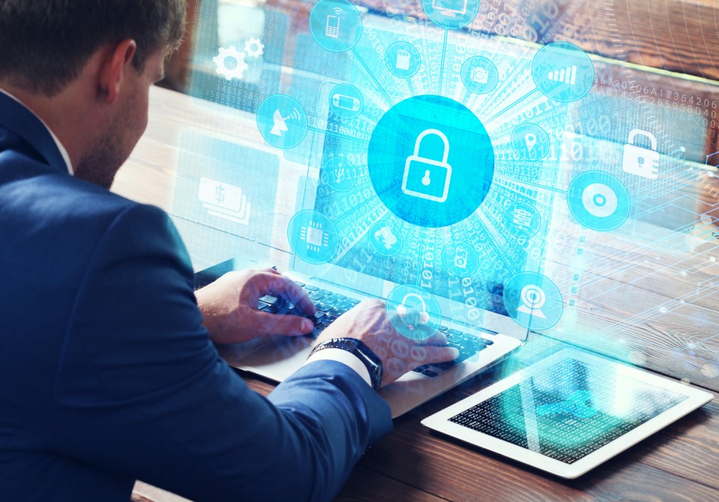 Young businessman working on his laptop in the office, select the icon security on the virtual display.